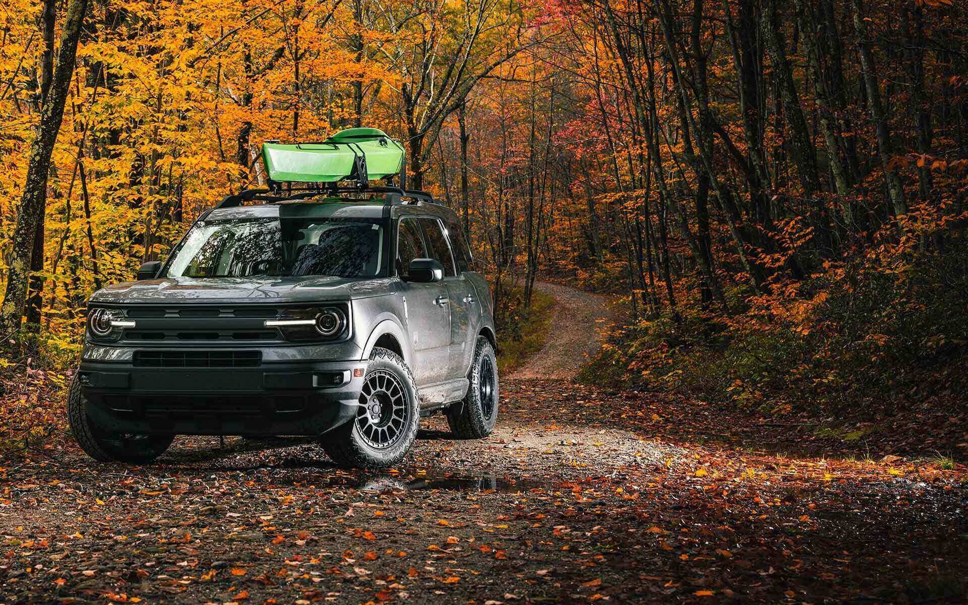 A black Land Rover with green kayak on roof pulls over on an autumn trail.